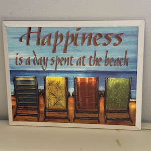 May include: A rectangular wall art piece with a white border. The artwork features the text "Happiness is a day spent at the beach" above a beach scene with four colorful beach chairs. The background shows a blue sky and ocean.