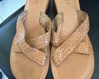 May include: A pair of light brown leather sandals with woven straps. The sandals have a wedge heel and the word "PAZZO" is printed on the footbed. The sandals are stitched with white thread around the edges.