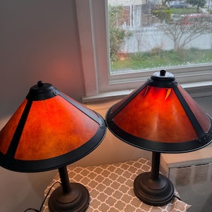 May include: A pair of table lamps with orange conical shades and black trim. The bases are dark brown and circular. The lamps are placed on a patterned grey and white surface. The lamps are indoors.