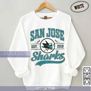 May include: White San Jose Sharks sweatshirt with teal and black graphic. The design includes the words "San Jose Sharks" and "EST. 2019". A shark logo is in the center. The sweatshirt is hanging on a wooden hanger.