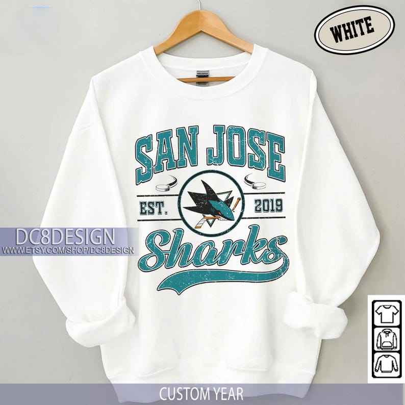 May include: White San Jose Sharks sweatshirt with teal and black graphic. The design includes the words "San Jose Sharks" and "EST. 2019". A shark logo is in the center. The sweatshirt is hanging on a wooden hanger.