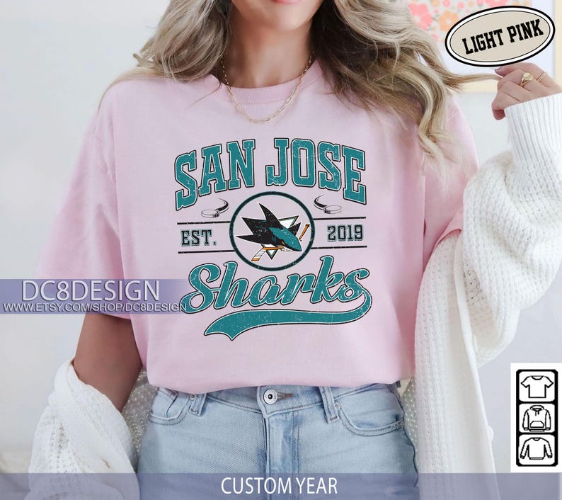 May include: Light pink t-shirt featuring the San Jose Sharks logo in teal and white. The design includes the text "SAN JOSE Sharks" and "EST. 2019". The shirt also has the text "DC8DESIGN" and "CUSTOM YEAR".