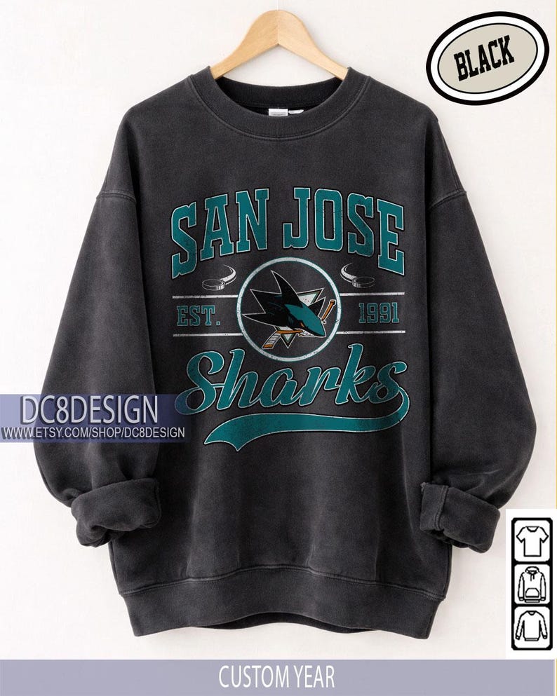 May include: Black San Jose Sharks sweatshirt with teal and white lettering and logo. The design includes "SAN JOSE" above "Sharks" and the year "1991". The sweatshirt is displayed on a hanger.