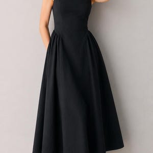 Pu&ograve; includere: Un abito midi nero senza maniche con scollo rotondo, corpetto aderente e una gonna ampia e plissettata che scende sotto le ginocchia. L'abito presenta un design pulito e a tinta unita con un punto vita strutturato e una silhouette semplice.