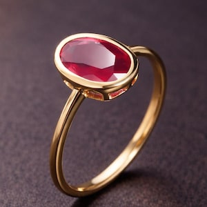 Peut inclure: Une bague en or ornée d'un grand rubis ovale. Le rubis est d'un rouge profond et est serti dans une lunette en or. Le corps de la bague est en or poli. La bague est présentée sur un fond sombre.