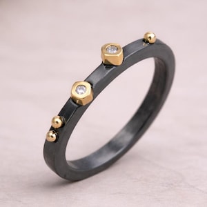 May include: A dark grey ring with gold accents. The ring features three gold-coloured, hexagonal shapes with small, clear stones and several gold spheres. The ring is a piece of jewellery.