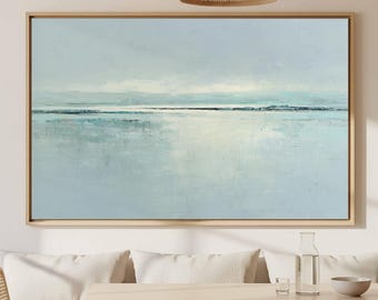 May include: A large rectangular landscape painting in a light wooden frame featuring an abstract seascape with soft shades of pale blue, white, and grey. The artwork depicts a calm horizon line with blended brushstrokes creating a serene water effect.