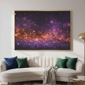 May include: A rectangular wall art piece featuring a dark purple and orange abstract bokeh light effect with shimmering glitter textures, framed in a thin gold border, displayed above a curved white sofa with blue and green throw pillows.