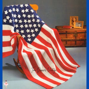 May include: A crocheted blanket featuring the design of the American flag with red and white horizontal stripes and a blue canton containing white star motifs. The blanket is draped over a wooden rocking chair. The text Tini Dancer Vintage is visible.