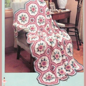 May include: A crochet blanket featuring a repeating hexagonal pattern in cream, dusty rose, and sage green. Each hexagon contains a raised, three-dimensional flower motif in the center. The edges are scalloped with a dusty rose and grey border. Text reads Tini Dancer Vintage.