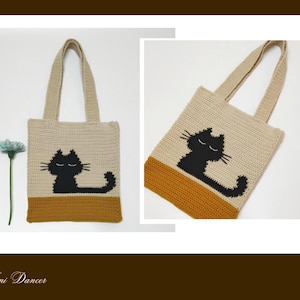 May include: A beige and mustard yellow crochet tote bag featuring a black cat graphic with closed eyes and long whiskers. The bag has two matching beige handles and a rectangular body. A small light blue flower is positioned next to the bag.