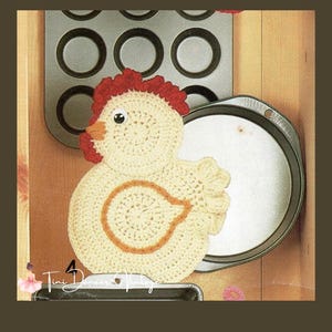 May include: A cream-colored crocheted chicken potholder featuring a red comb and wattle, an orange beak, and a black and white eye. The chicken has a circular body with an orange outline and a textured tail. The text Tini Dancer Vintage is visible.