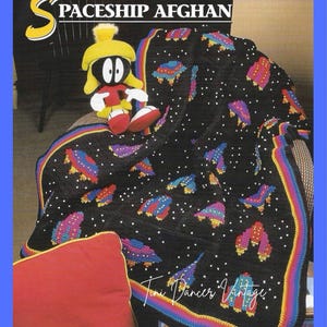 May include: A black crocheted afghan blanket featuring colourful spaceship motifs and white star accents, with a rainbow-striped border. The text SPACESHIP AFGHAN appears at the top, and the text Toni Dancer Vintage is at the bottom.