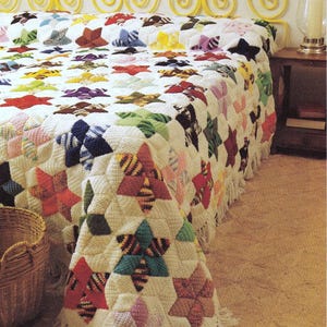 May include: A crocheted bedspread featuring a repeating pattern of multi-colored star motifs on a white background. The stars are crafted in various solid and striped yarn colors including red, blue, green, yellow, and pink. The edges feature fringe.