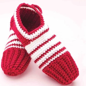 Peut inclure: Une paire de chaussons crochetés à la main présentant un motif rayé rouge et blanc vif. Les chaussons sont fabriqués avec un fil épais et texturé, mettant en valeur un design côtelé sur tout le corps et une section rouge unie au bout et au talon.