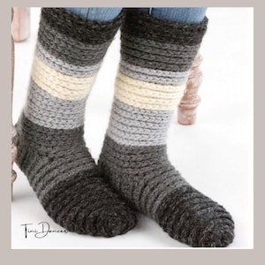 Puede incluir: Un par de calcetines de punto a media pantorrilla con rayas horizontales en tonos gris oscuro, gris claro y crema. Los calcetines tienen una construcción de hilo grueso y texturizado, con el texto Tini Dancer impreso en negro en la esquina inferior izquierda.