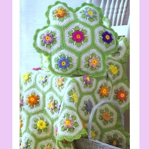 Puede incluir: Un cojín y una manta de ganchillo con un patrón hexagonal de centros blancos, bordes verde claro y pequeñas flores tridimensionales en varios colores como amarillo, naranja, rosa, morado y azul, con un borde festoneado.