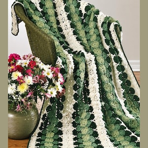 May include: A crocheted blanket featuring vertical stripes in alternating shades of dark green, light green, and cream. The pattern consists of repeating circular motifs connected by openwork stitching, creating a textured, layered appearance.