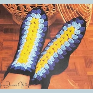 Puede incluir: Un par de zapatillas tejidas a mano con un patrón de granny square en hilo amarillo brillante, azul claro y azul oscuro. Las zapatillas tienen una base negra sólida y un diseño de rayas verticales centrales a lo largo del empeine.