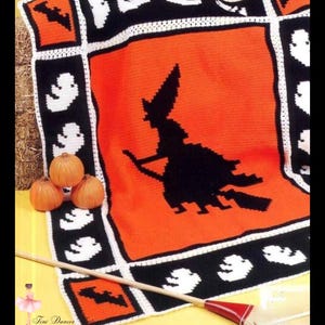 Puede incluir: Una manta de Halloween tejida a ganchillo con una silueta de bruja negra sobre un fondo naranja. La manta tiene un borde negro con motivos de fantasmas y murciélagos blancos. También se ven tres pequeñas calabazas y una escoba.