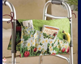 May include: A walker bag with a floral print pocket and a green top. The pocket is filled with tissues, a book, and a banana. The bag is attached to a silver walker frame with red ties.