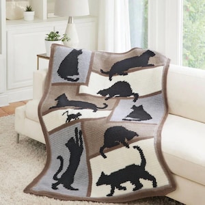 Può includere: Una coperta all'uncinetto con un design patchwork. Presenta sagome di gatti neri su una tavolozza neutra di bianco, grigio e marrone. La coperta è drappeggiata su un divano bianco, mettendo in risalto la sua consistenza accogliente e il motivo a tema gatto.