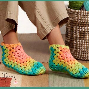 May include: A pair of ankle-high crochet slippers featuring a vibrant granny square pattern in shades of orange, yellow, green, and blue. The slippers have a textured, open-stitch design and are labeled with the text Tini Dancer in the bottom corner.