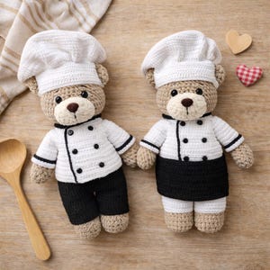 K&ouml;nnte beinhalten: Zwei geh&auml;kelte Teddyb&auml;ren als K&ouml;che verkleidet. Jeder B&auml;r tr&auml;gt eine wei&szlig;e Kochm&uuml;tze, eine wei&szlig;e Jacke mit schwarzen Kn&ouml;pfen und Verzierungen sowie entweder eine schwarze Hose oder eine schwarze Sch&uuml;rze. Die B&auml;ren befinden sich auf einer Holzoberfl&auml;che.