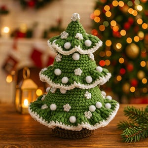 Puede incluir: Un árbol de Navidad de ganchillo verde hecho a mano con ribetes blancos y pompones blancos decorativos y adornos en forma de flor. El árbol está sobre una base marrón, una decoración festiva.