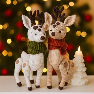 Puede incluir: Dos figuras de renos de ganchillo hechos a mano. Uno es blanco con una bufanda verde, el otro es marrón con una bufanda roja. Ambos tienen cuernos y manchas marrones. Son decoraciones navideñas, con una vela y un árbol de Navidad de fondo.