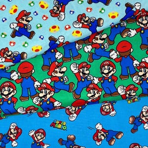 May include: Three layers of fabric featuring Super Mario character prints. The top layer is light blue with Mario and mushrooms, the middle is green with Mario figures, and the bottom is bright blue with Mario and the Super Mario logo text.