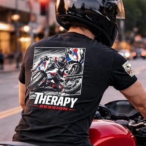 Könnte beinhalten: Eine Person fährt mit einem roten Motorrad durch eine Stadt. Der Fahrer trägt einen schwarzen Helm und ein schwarzes T-Shirt mit dem Aufdruck "THERAPY SESSION" auf dem Rücken. Das Motorrad hat einen schwarzen Reifen und Auspuff.