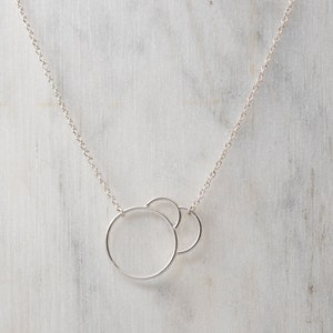 Peut inclure: Un collier en chaîne argent avec deux cercles entrelacés comme pendentif.