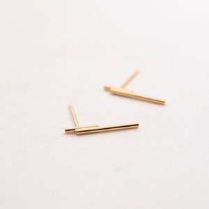 May include: A pair of gold bar stud earrings. The earrings are made of two thin gold bars that are stacked on top of each other.