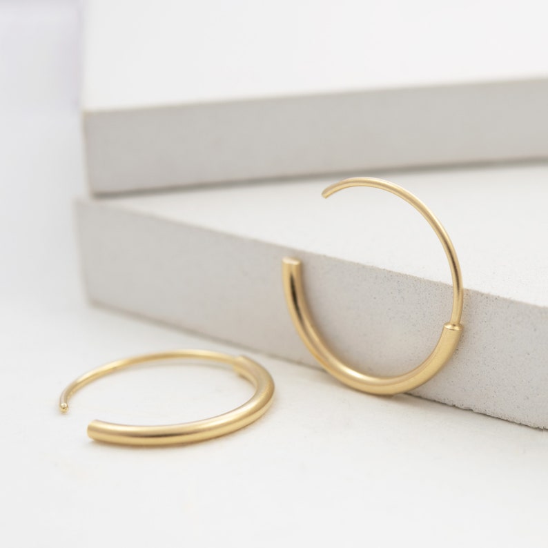 May include: A pair of gold hoop earrings. The earrings are simple and elegant, with a smooth, rounded finish.