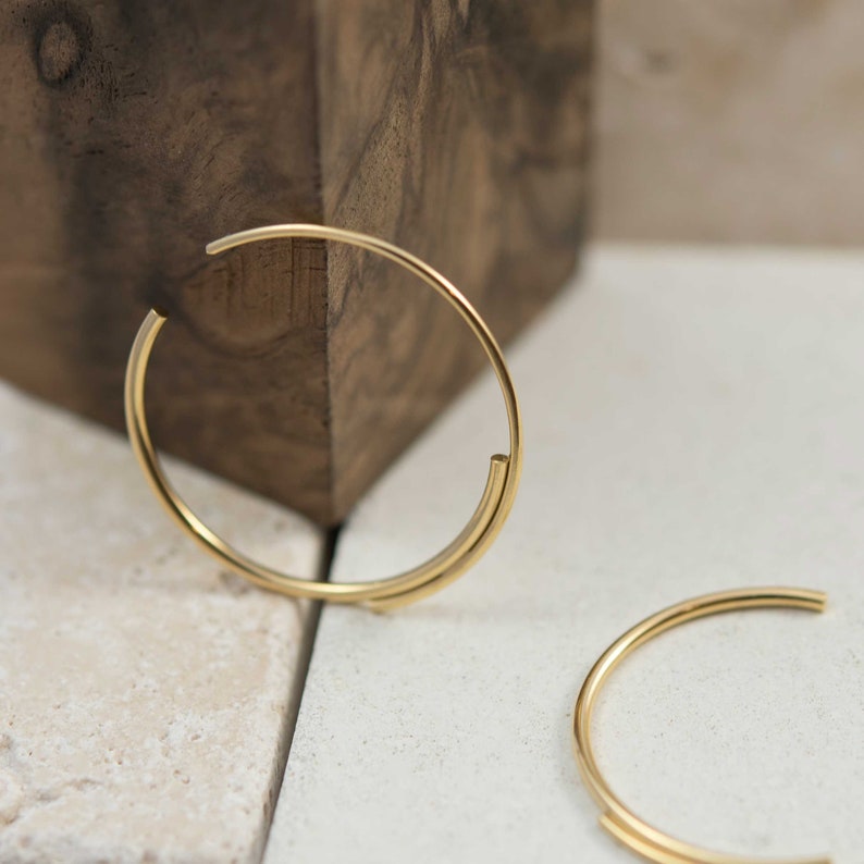May include: A pair of gold hoop earrings with a unique design. The hoops are made of two thin pieces of metal that are joined together at the top and bottom. The earrings are simple and elegant, and would make a great addition to any jewelry collection.