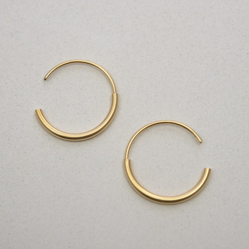 May include: A pair of gold hoop earrings. The hoops are thick and have a smooth, polished finish.