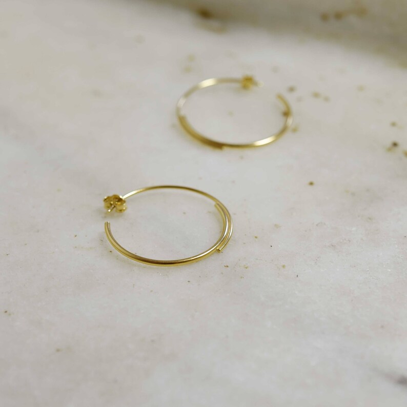 May include: A pair of gold hoop earrings. The earrings are simple and elegant, with a thin, delicate design.