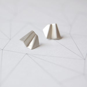 May include: A pair of silver geometric earrings with a folded paper design.