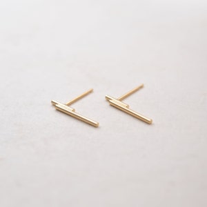 May include: A pair of gold bar stud earrings. The earrings are made of two thin gold bars that are stacked on top of each other.