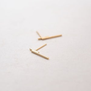 May include: Two pairs of gold bar stud earrings. The earrings are simple and minimalist.
