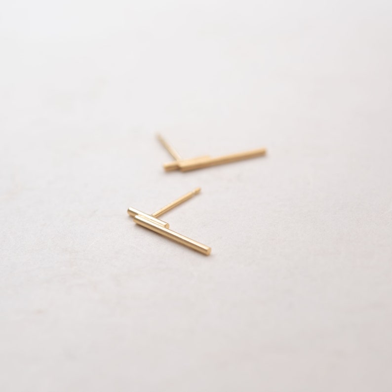 May include: Two pairs of gold bar stud earrings. The earrings are simple and minimalist.
