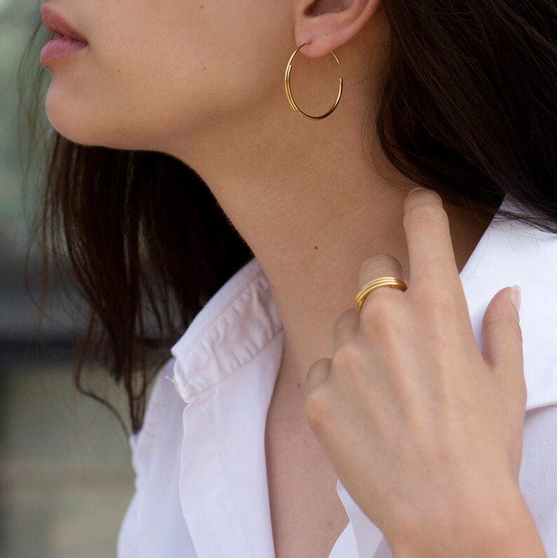 May include: A woman wearing a white shirt with gold hoop earrings and a gold ring on her finger.