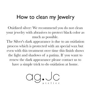May include: Text explaining how to clean oxidized silver jewelry. The text recommends not using abrasives to protect the black color. It also explains that the dark appearance is due to an oxidation process protected by a special wax. The text also mentions that the finish shows light and shadows of a patina over time. The text concludes by saying that if you want to renew the dark appearance, you can contact the company for a simple trick to do oxidation at home. The text is followed by the company name "ag.Jc atelier".