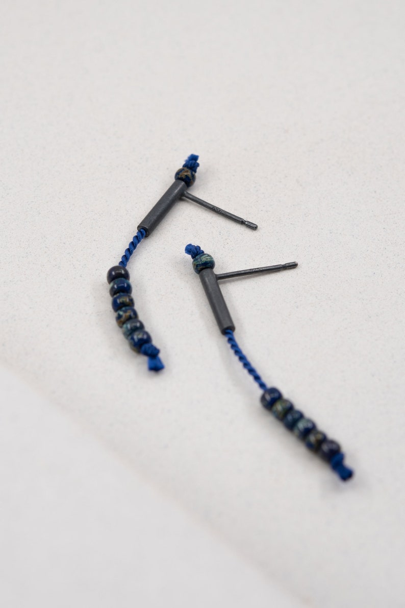 Pair of 38 mm length pendant earrings handmade in oxidized sterling silver tube with a blue silk cord threaded through the center for hanging Miyuki beads in Picasso cobalt blue. Designed and crafted by hand in Paris by A g J c