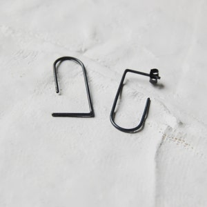 May include: A pair of black metal earrings with a simple geometric design. The earrings are made of thin wire and have a slightly curved shape.