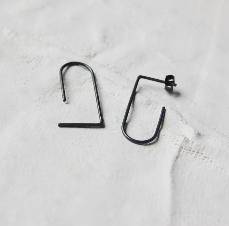 May include: A pair of black metal earrings with a simple geometric design. The earrings are made of thin wire and have a slightly curved shape.