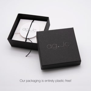 May include: Black jewelry box with a white label that says "ag.jc jewelry". The box is closed and the lid is open, revealing a white tissue paper interior.
