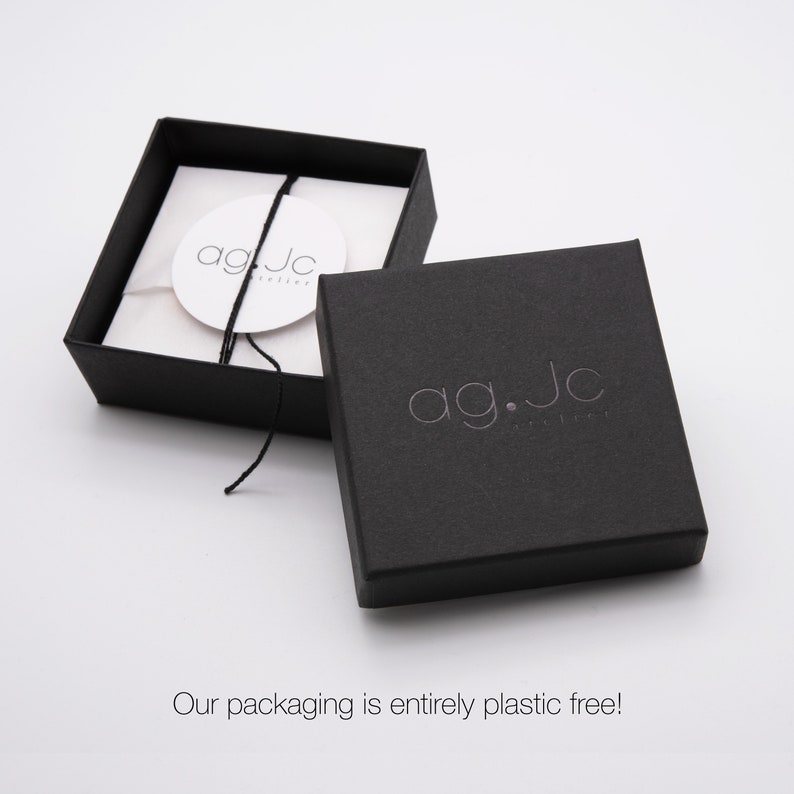 May include: Black jewelry box with a white label that says "ag.jc jewelry". The box is closed and the lid is open, revealing a white tissue paper interior.