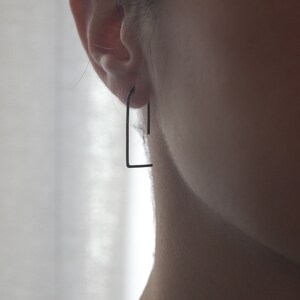 May include: A pair of black minimalist hoop earrings. The earrings are made of thin metal and have a simple, geometric design.